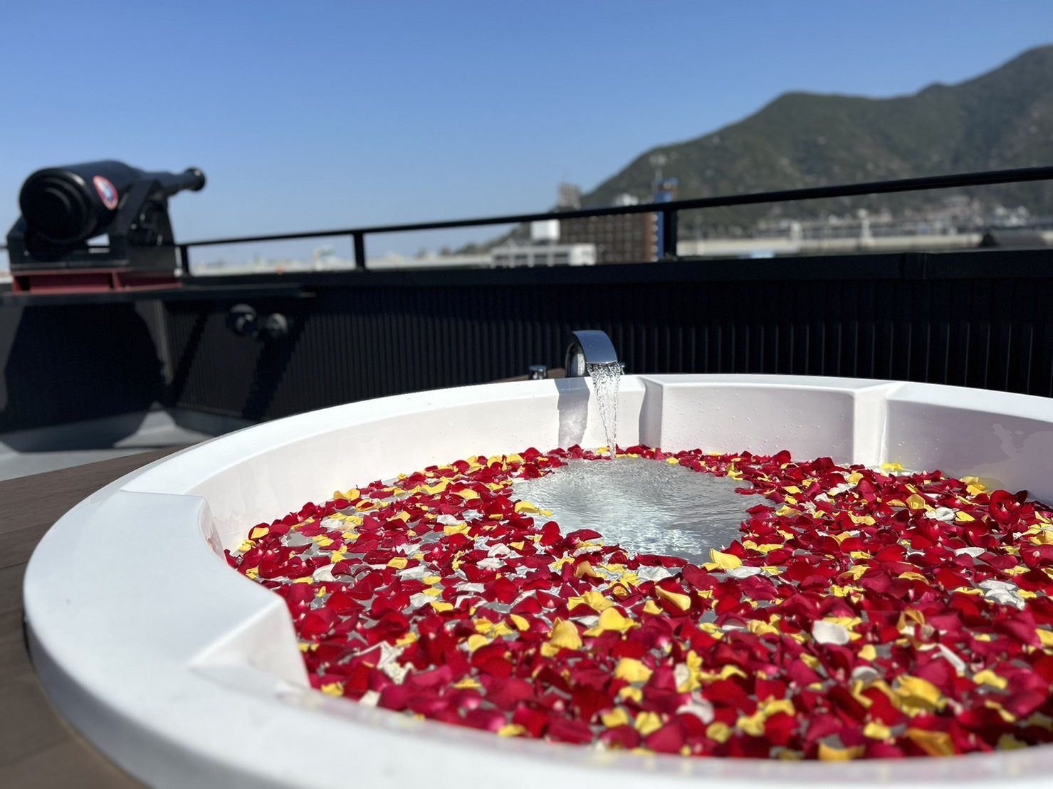 バラの花びらを一面に浮かべた屋上のジャグジーバス。奥にクロフネ砲と山